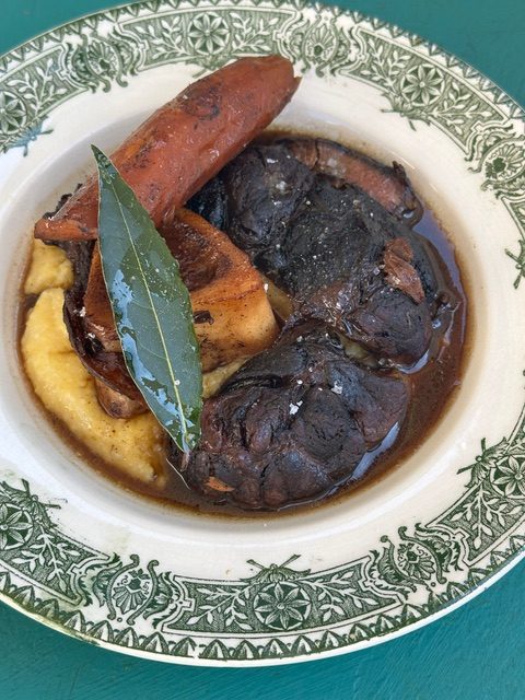 Braised beef shank with polenta and laurel jus, on a green-rimmed plate